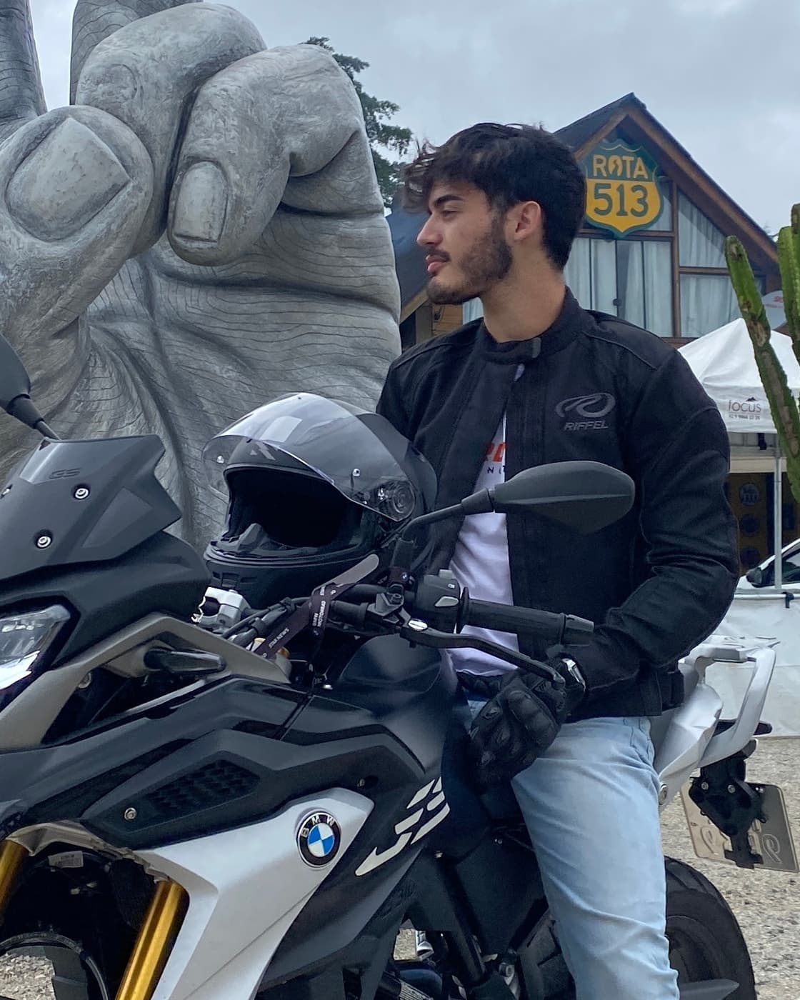 Agnaldo Guerra sitting on a motorcycle at a roadside stop, helmet resting on the handlebars.